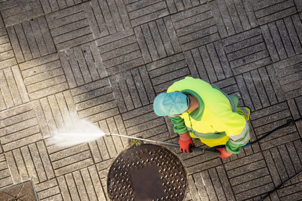 Worker cleaning a street sidewalk with high pressure water jet machine on sunny day Copy space Top view