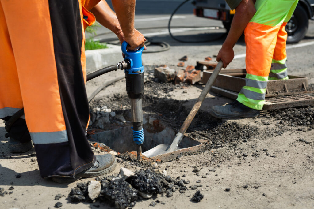 A road worker is dismantling street asphalt and old drainage with a jackhammer